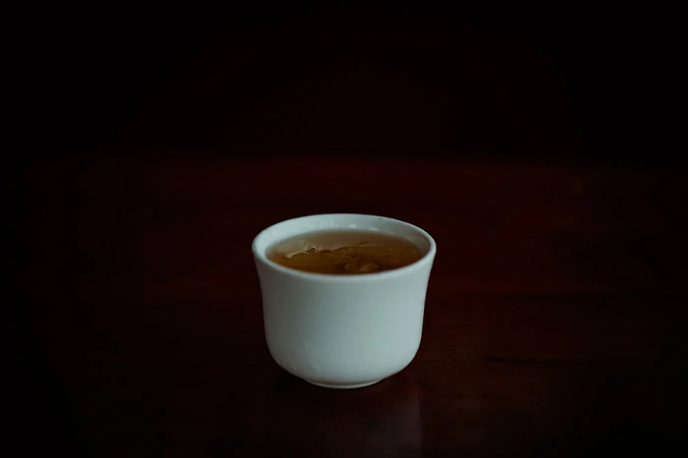 極簡風格的瓷杯盛滿黃亮茶湯，深色背景襯托出溫暖色澤 | A minimalist porcelain cup filled with yellow tea liquor against a dark background